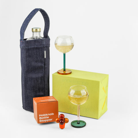 Wine denim tote, an amber bottle stopper and it's box and two wine glasses on a wrapped box