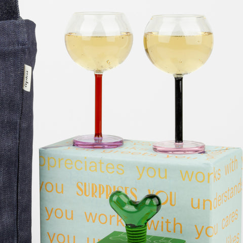 Close up of two wine glasses on a wrapped box, a green wine stopper and a denim tote