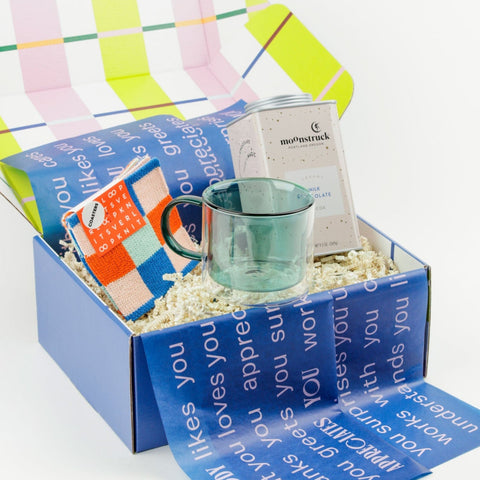 Teal glass mug with hot chocolate tin and colorful coasters in a gift box