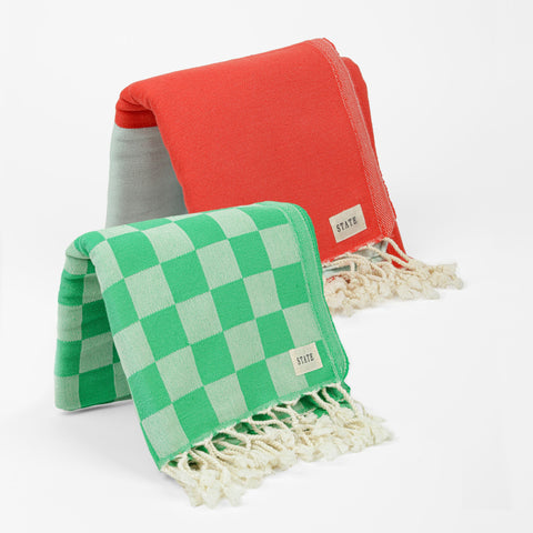 One green checkered towel with tassels and one red and blue towel with tassels