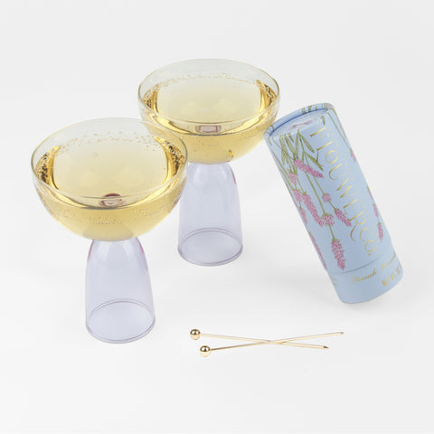 2 clear and lavender coupes with ginger liquid, two cocktail picks and a lavender tube of cocktail cubes leaning against a coupe