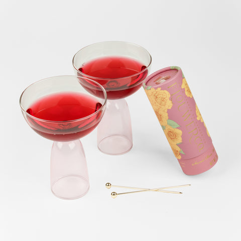 2 clear and pink coupes with red juice, two gold cocktail picks and one pink tube of cocktail cubes