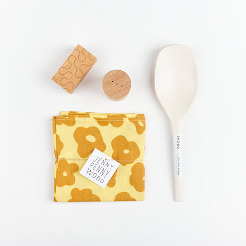 Areaware Pattern Salt and Pepper Shakers, a set of white EKOBO Bamboo serving spoons, and a yellow and orange floral patterned Jenny Pennywood cotton linen Everywhere Square