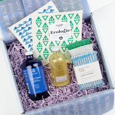 an open gift box showing a set of cool colored lurex sponges, two Swedish dish clothes, a blue bottle of all purpose cleaning spray and a bottle of hand soap