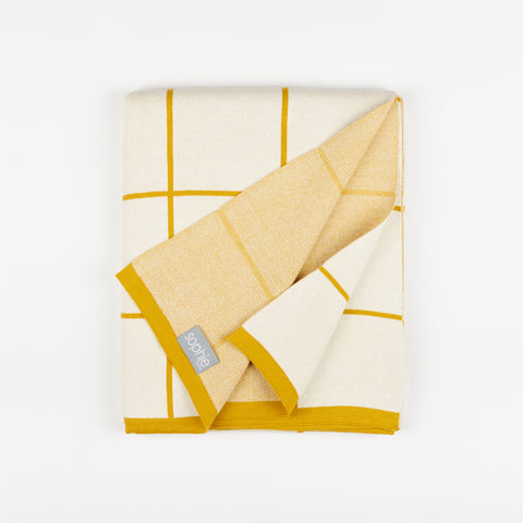 Sophie Home grid cotton knit throw blanket in citrus with one corner lifted up showing the tag and the underside of the blanket