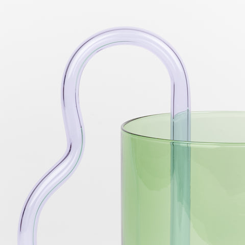 a detail of a green borosilicate glass pitcher with a lilac curving glass handle