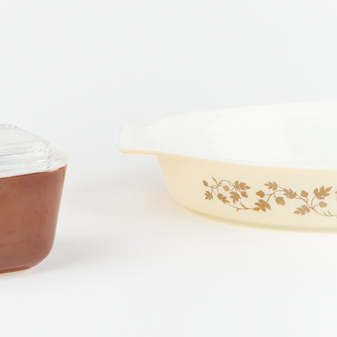 close up view of Vintage set of two Pyrex serving dishes. One is smaller and comes with a glass lid and the other is larger and has a brown oak leaf design on it.