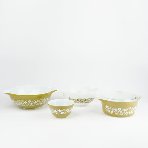 A set of four vintage Pyrex bowls with a floral wrap around design and have an avocado color