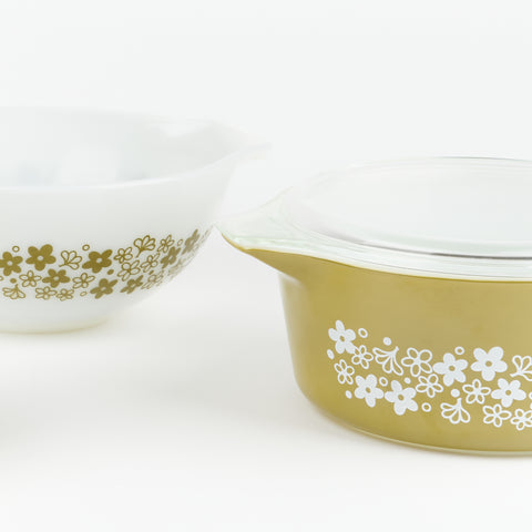 a close up of two pyrex bowls one is white with a green floral design and the other is green with a white floral design and a glass lid