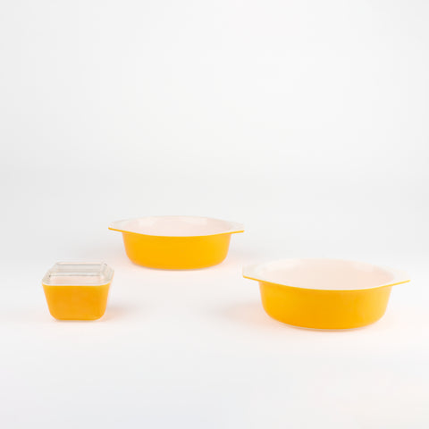 a set of bright yellow vintage pyrex serving bowls. two bowls are larger and one is smaller and has a glass lid cover