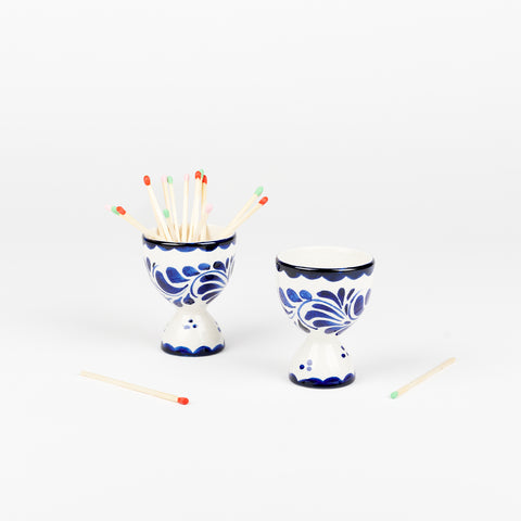 pair of blue and white ceramic egg cups with matches sticking out of one of the cups