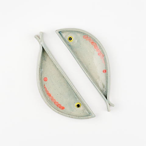 Two handmade ceramic fish shaped dishes laying close to each other but pointing in opposite directions
