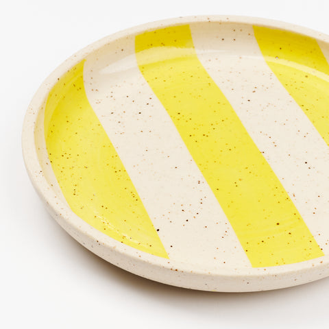 a close up view of a speckled ceramic plate with yellow stripes