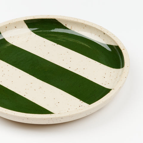 A close up view of a handmade speckled ceramic plate with three dark green stripes