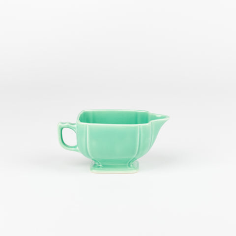 a pale green ceramic milk creamer with a handle and a decorative foot