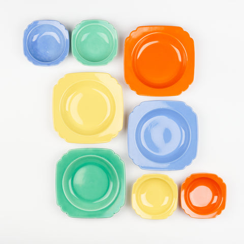 eight vintage ceramic bowls arranged artfully on a white backdrop four are large and four are small they are red, yellow, blue and green