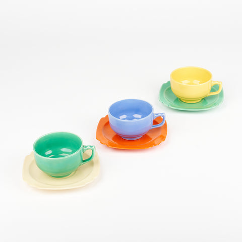 Three colorful tea cups on saucers diagonally lined up. green cup on yellow saucer blue cup on red saucer yellow cup on green saucer