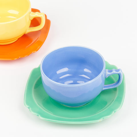 Two colorful ceramic tea cups and saucers. A blue tea cup on a green saucer and a yellow tea cup slightly out of the frame sitting on a bright red saucer plate
