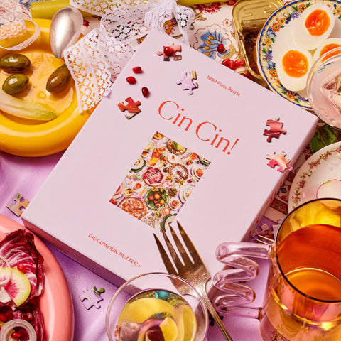Lavender Cin Cin Piecework Puzzle 1000 piece puzzle box surrounded by cocktails, finger foods, lace ribbon, and puzzle pieces
