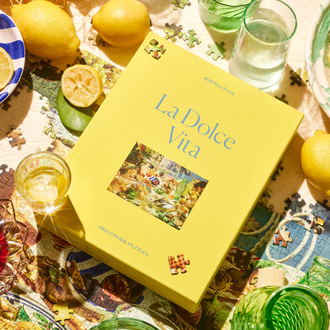 Yellow La Dolce Vita Piecework Puzzle 1000 piece puzzle box surrounded by colorful glassware, lemons, and puzzle pieces