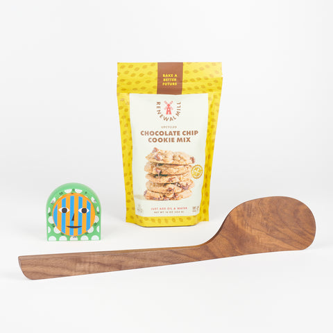 An Areaware Kitchen Timer next to a yellow bag of Renewal Mill Chocolate Chip Cookie Mix, and a Bad Dogs Studio Walnut spatula