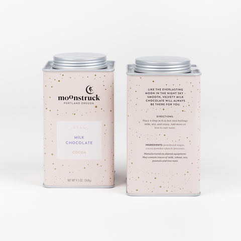 Two tins of Moonstruck Milk Chocolate cocoa mix one showing the front side and the other showing a side view of the tin with ingredients and directions for use