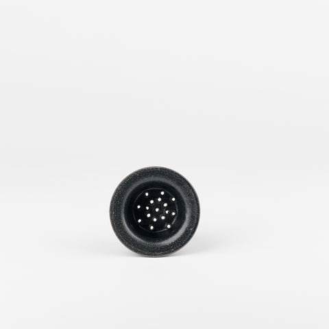 a black ceramic tea strainer handmade by Utility Objects laying on its side