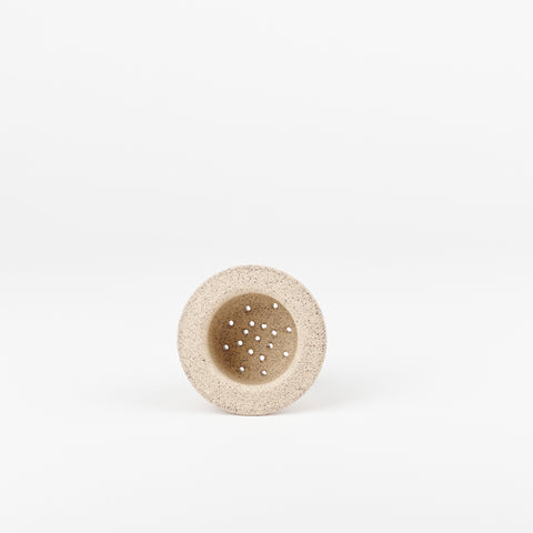 a sand colored ceramic tea strainer handmade by Utility Objects laying on its side