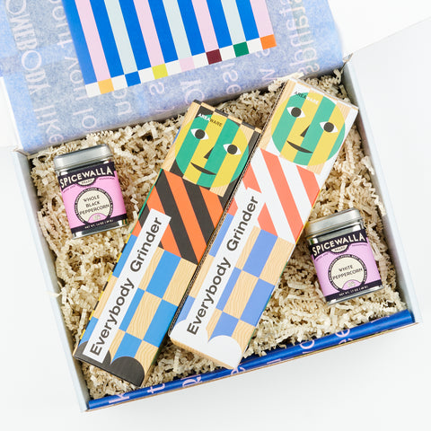 An open gift box showing two Areaware Everybody Grinders and two tins of Spicewalla whole black and white peppercorns