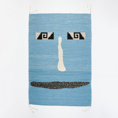 A hand-woven blue abstract face rug or wall hanging made in Mexico a designed by Amanda Barr