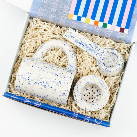 an open Cette gift box featuring a set of blue speckled ceramic pieces including a mug, tea strainer, and coffee scoop