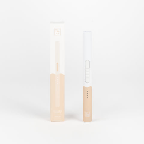 A Botanica Duo Tone Flameless lighter in standing upright next to the box that it comes in with a two tone white and natural mauve color