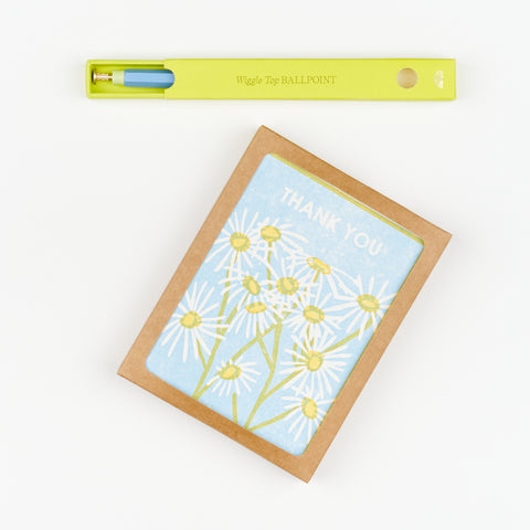 A gift set that includes a Box of Thank You Cards with a floral design featuring daises and a yellow box with a blue pen inside it