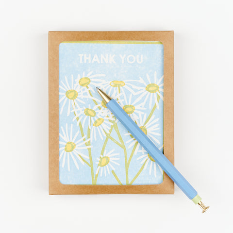 A blue Papier wiggle top pen sitting on top of a box of daisy floral themed thank you cards