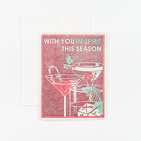 A blank holiday notecard with an illustration of cocktail glasses, a candy cane, and greenery that reads "With you in spirit this season" on the front of the card
