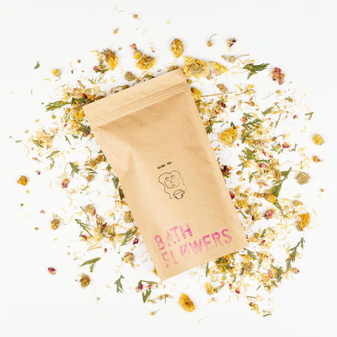 a brown bag of Masha Tea Bath Flowers with hand printing sitting on top of a spray of dried wildflowers
