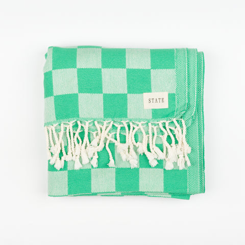 a folded green checkerboard towel with tassels and a small tag that reads State