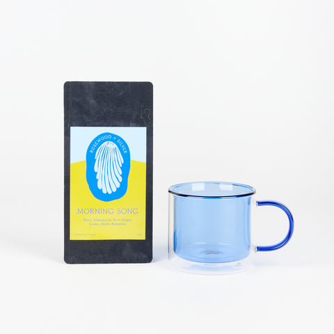 A Poketo Double Wall Mug in Blue next to a black bag of Rosewood + Silver Tea called Morning Song with a blue and yellow label