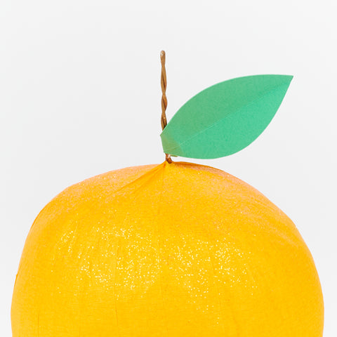 A detailed close up of a paper orange with glitter on the surface and a green paper leaf