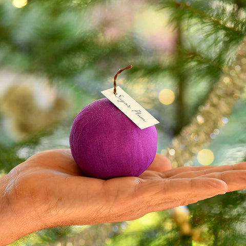 Purple "sugar plum" surpise ball held in a hand with a blurred festive background