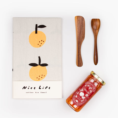 Flat lay of Jam On It gift set items: artisanal marmalade, tea towel, and walnut spreaders—perfect for thank you and host gifts.
