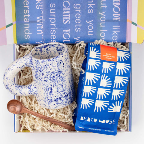 Morning Tide gift set with bag of small-batch coffee, handmade ceramic mug in speckled blue, and a walnut stirring spoon, arranged in an open gift box.