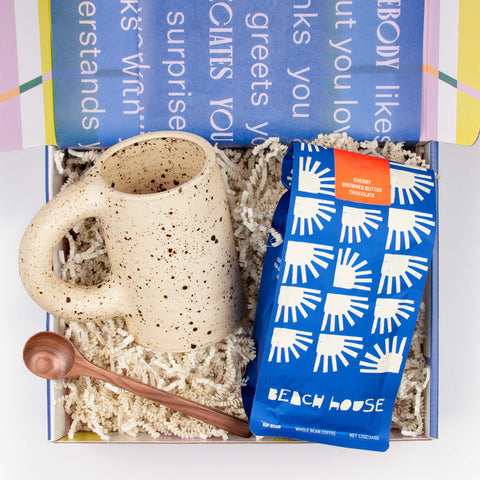 Morning Tide gift set with bag of small-batch coffee, handmade ceramic mug in eggshell, and a walnut stirring spoon, arranged in an open gift box.