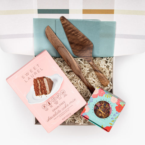 Petal & Plume gift set with a box of Sweet Laurel chocolate cake mix, a set of walnut cake servers, and tin of Flouwer Co. edible flower petals, arranged in an open gift box—perfect for weddings or milestone celebrations.