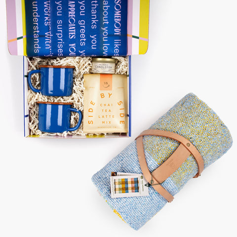 Kindled Comfort gift set with handwoven blanket beside the chai tea, enamel mugs, and candle travel tin arranged in a gift box on a white background.