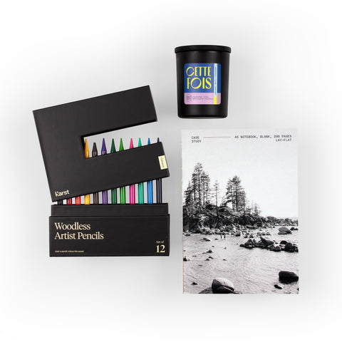 Overhead view of the True Colors gift set featuring a blank Case Study notebook, a CETTE Fois candle, and Karst woodless artist pencils with the back box partially open to reveal an array of colorful pencils.