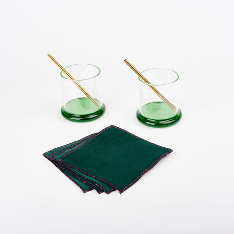 A pair of Sophie Lou Jacobsen fritter glasses with green bases, two metal cocktail straws and a set of four green velvet Atelier Saucier cocktail napkins