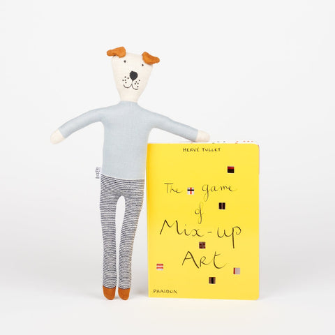 A Sophie Home stuffed animal toy dog in blue standing and leaning on a copy of Phaidon Kids book The Game of Mix-Up Art a