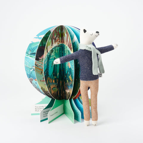 A Sophie Home Kids stuffed animal Polar Bear standing next to an open view of the globe-shaped children's book Our Underwater World