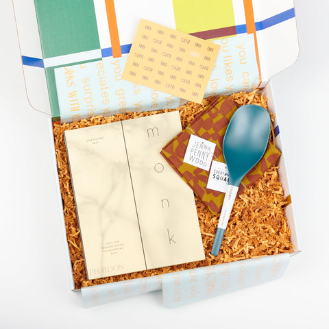 An open Cette Gift Box including Blue Abyss EKOBO bamboo serving spoons, Phaidon Cookbook - Monk: Light and Shadow on the Philosophers Path, and a Jenny Pennywood Everywhere Square in a checks pattern in maroon and ocher